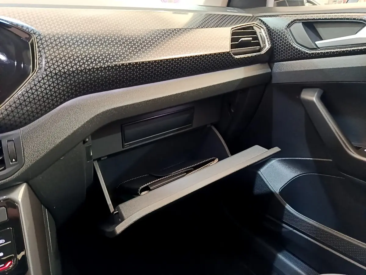 Intérieur noir du Volkswagen T-Cross 2022, vue sur la boîte à gants ouverte côté passager avec tableau de bord texturé.