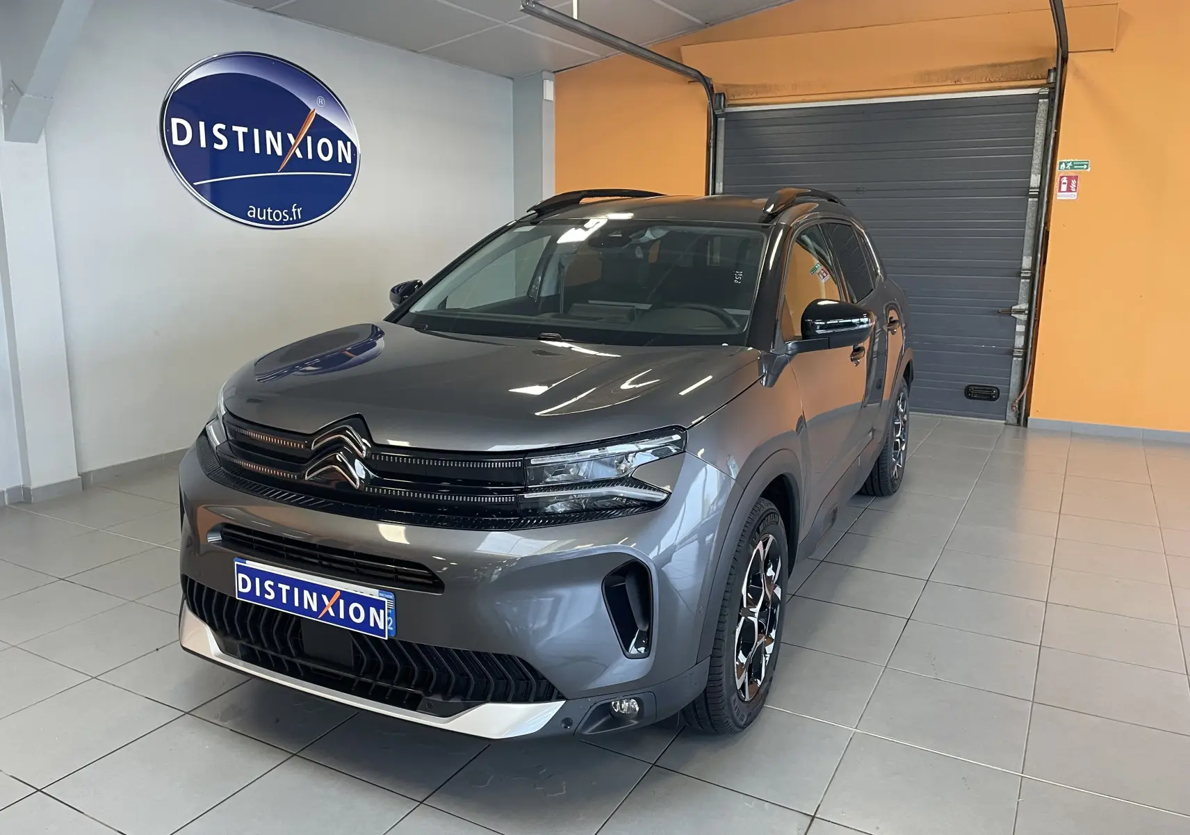 Vue 3/4 avant d'un Citroën C5 Aircross hybride gris platinium avec jantes biton et toit noir en showroom.