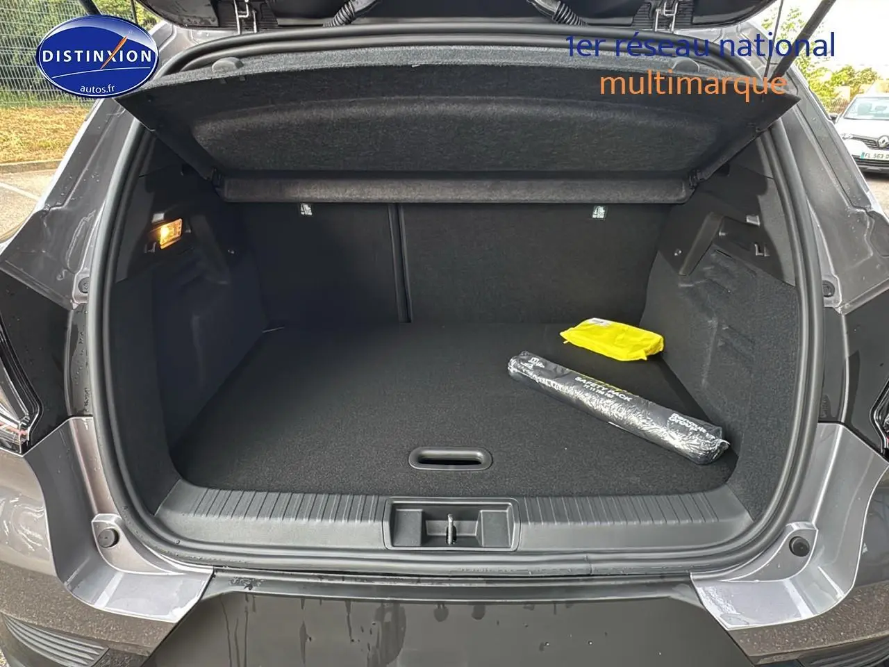 Coffre ouvert vu de l'arrière d'un Renault Captur gris cassiopée avec tapis noir et objets posés à droite