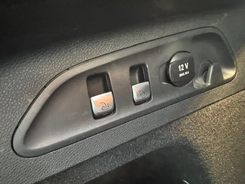 Gros plan sur les commandes d'ouverture du coffre et prise 12V dans le coffre du Mercedes GLC Coupé blanc polaire.