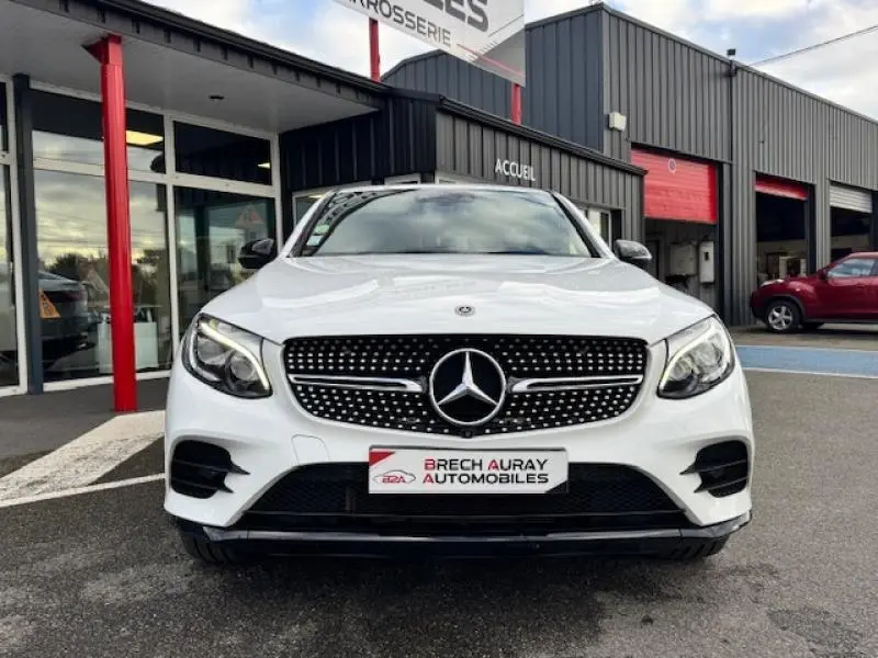 Vue frontale d'un Mercedes GLC Coupé blanc polaire avec calandre diamantée et phares LED allumés.