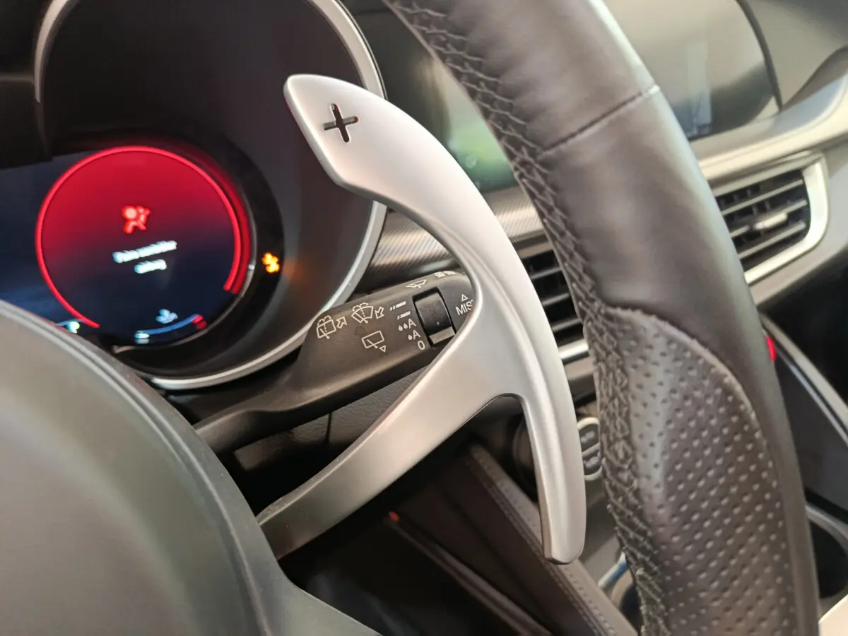 Gros plan sur la palette de changement de vitesse alu côté droit du volant cuir perforé d’un Alfa Romeo Stelvio gris foncé.