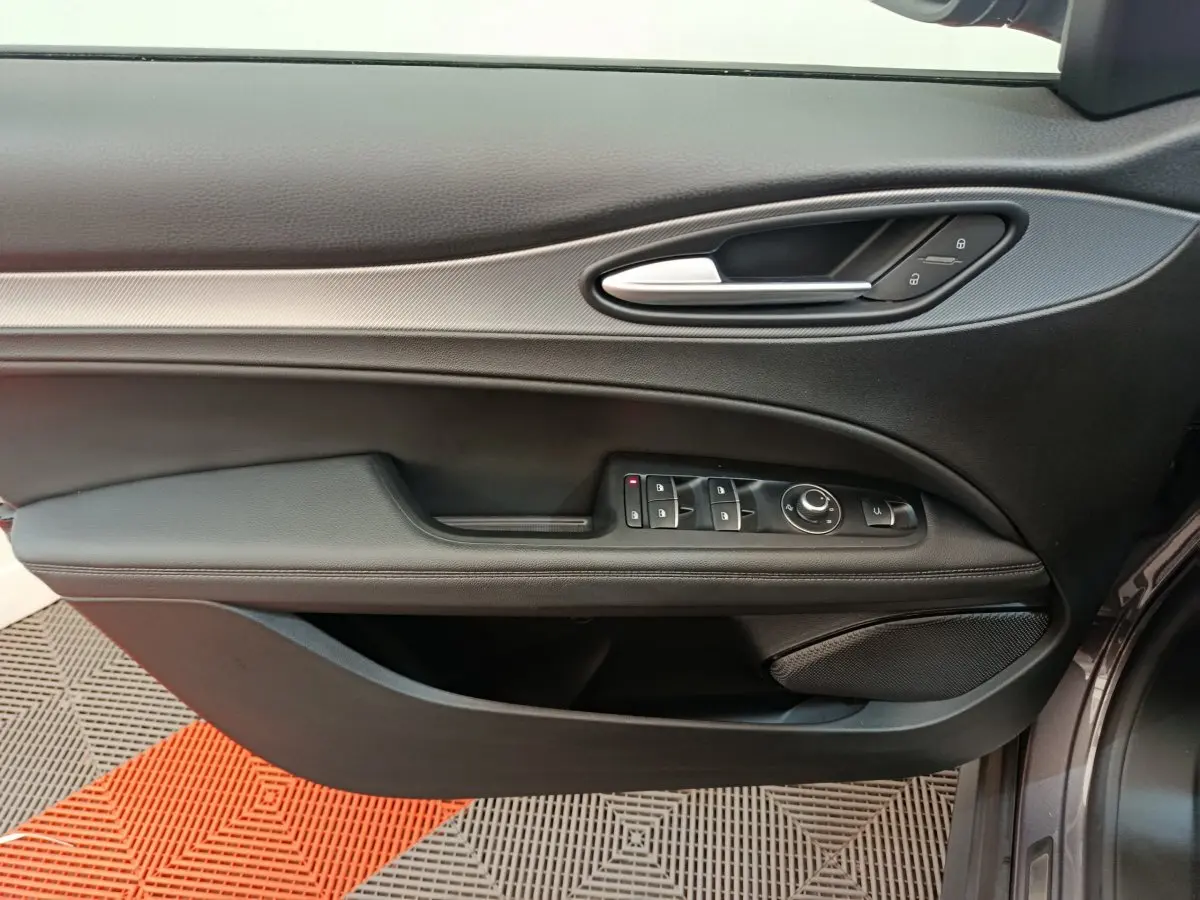 Vue rapprochée de la porte avant gauche de l'Alfa Romeo Stelvio gris foncé, avec commandes électriques et poignée argentée.