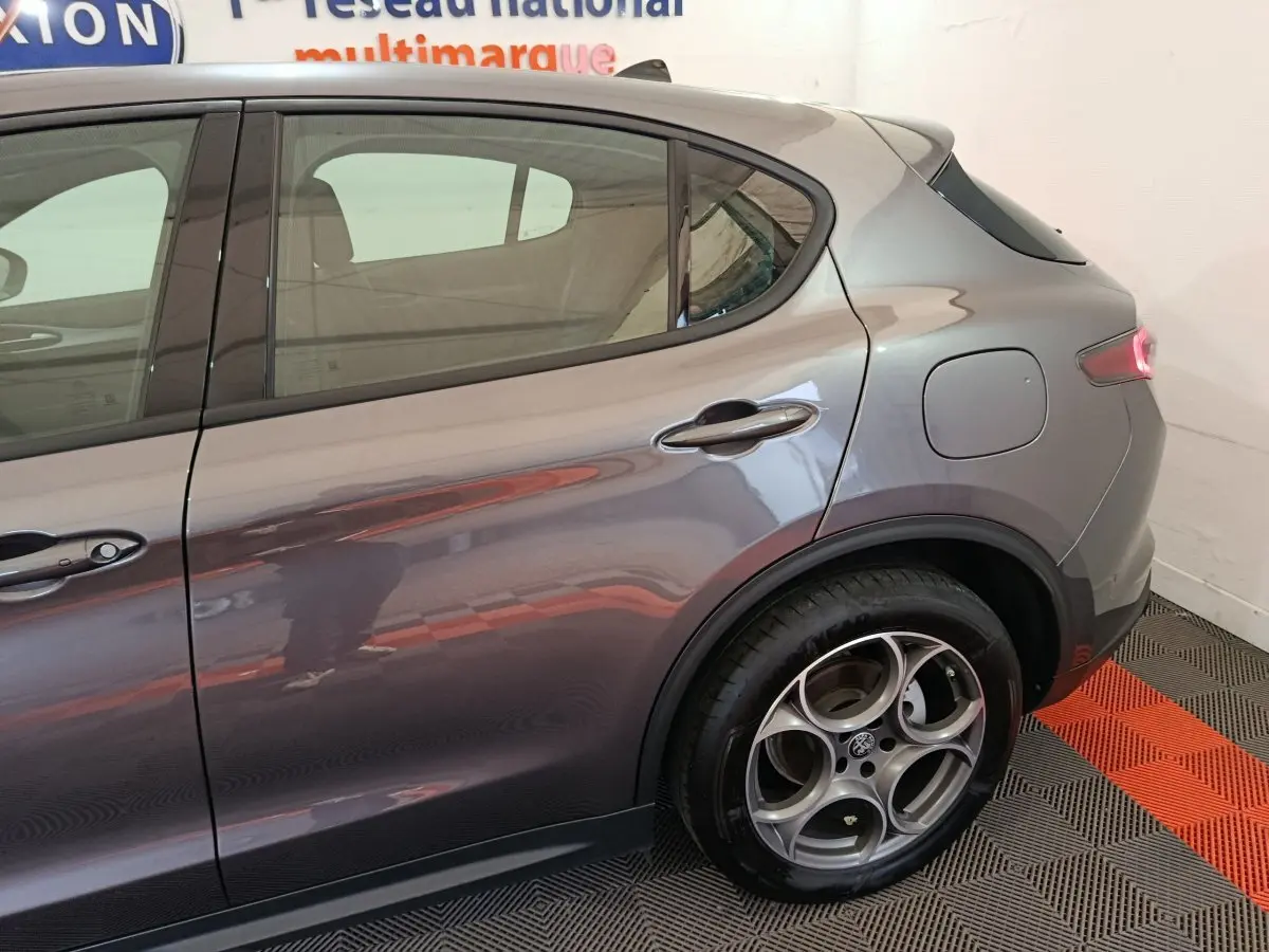 Vue latérale arrière droite d’un Alfa Romeo Stelvio gris foncé, mettant en valeur la jante spécifique et la trappe à carburant.