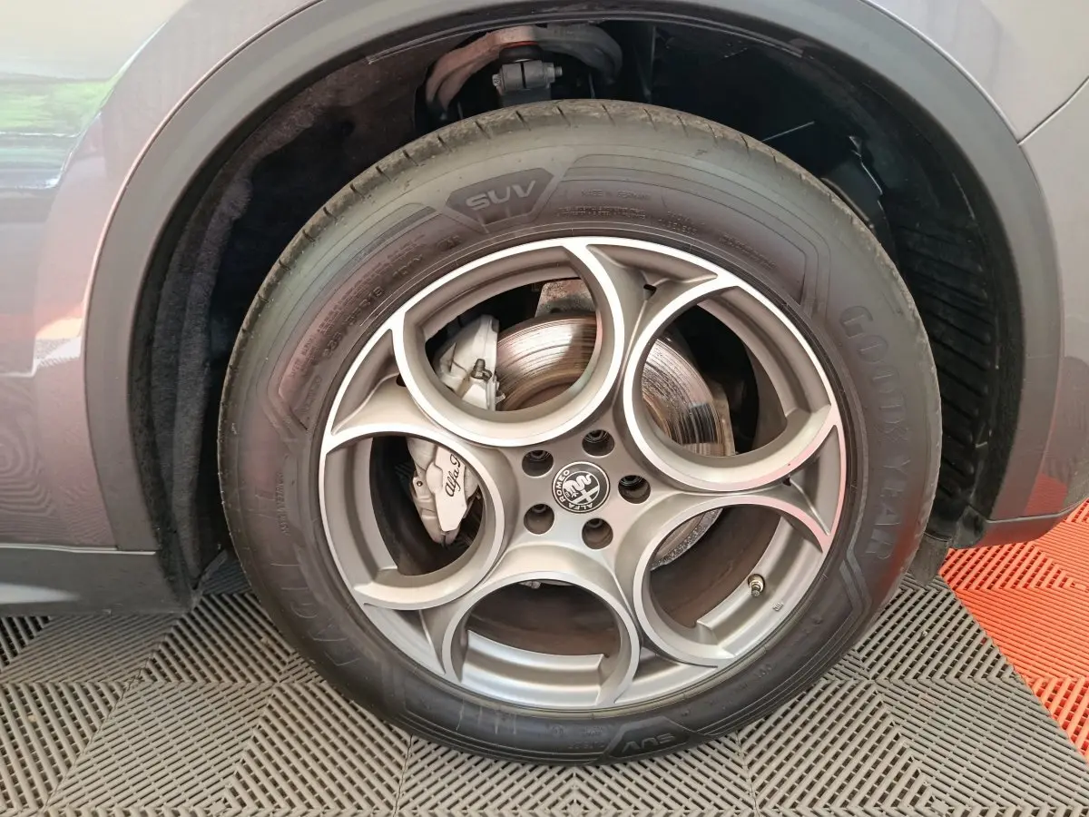 Gros plan sur la roue avant droite gris foncé de l'Alfa Romeo Stelvio 2.2 TD 160 AT8 Sprint avec jante distinctive à cinq cercles.