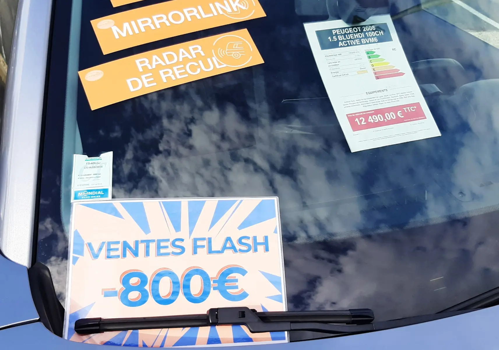 Vue avant rapprochée du pare-brise gris Artense d’un Peugeot 2008 2020 avec affiches promotionnelles et étiquettes techniques.