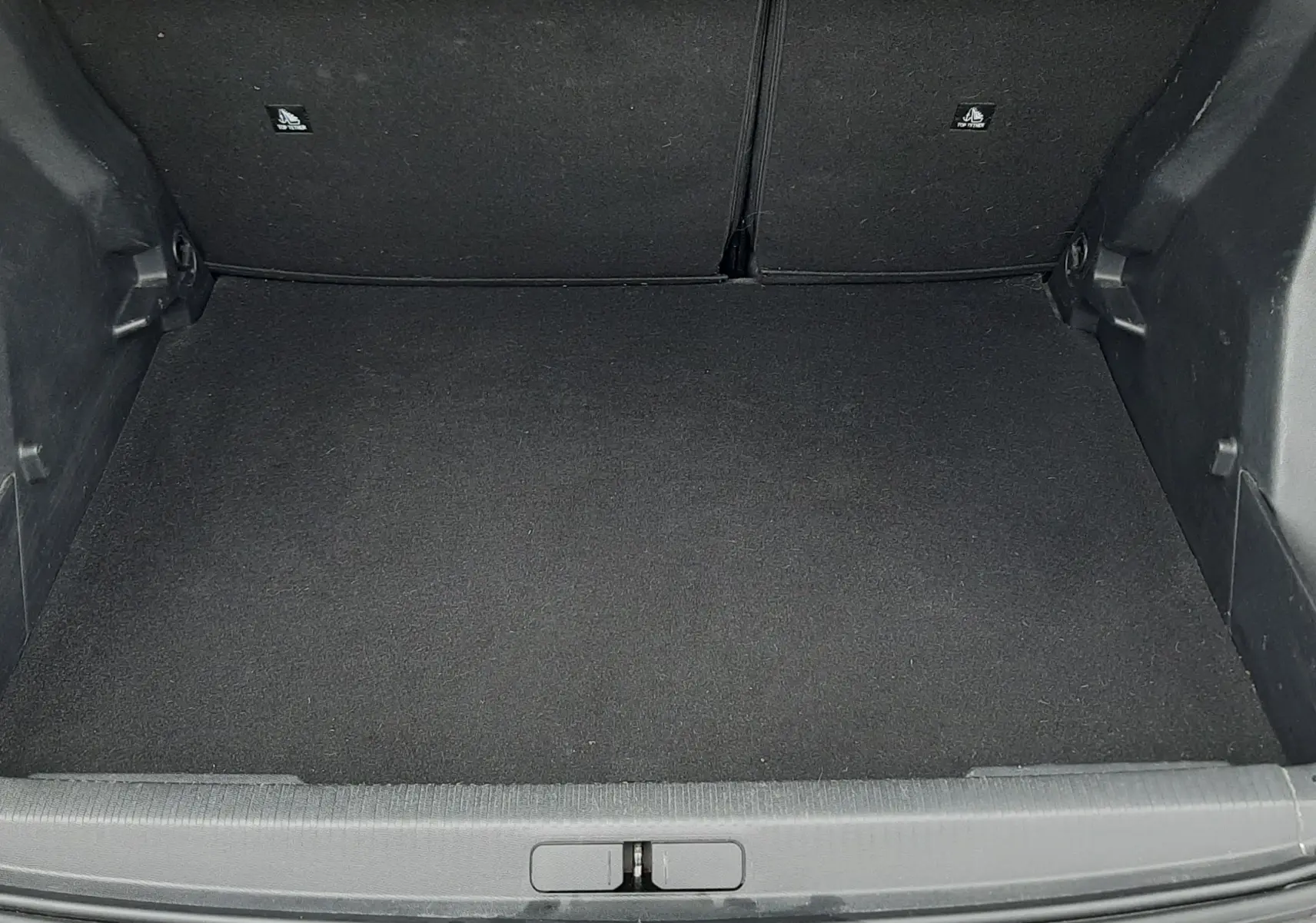 Vue plongeante sur le coffre vide du Peugeot 2008 gris Artense, montrant la moquette noire et les parois intérieures.