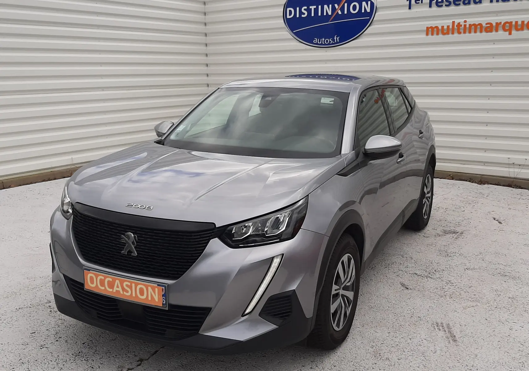 Peugeot 2008 gris Artense vue 3/4 avant droit, avec calandre noire et feux LED distinctifs, en extérieur sur parking.