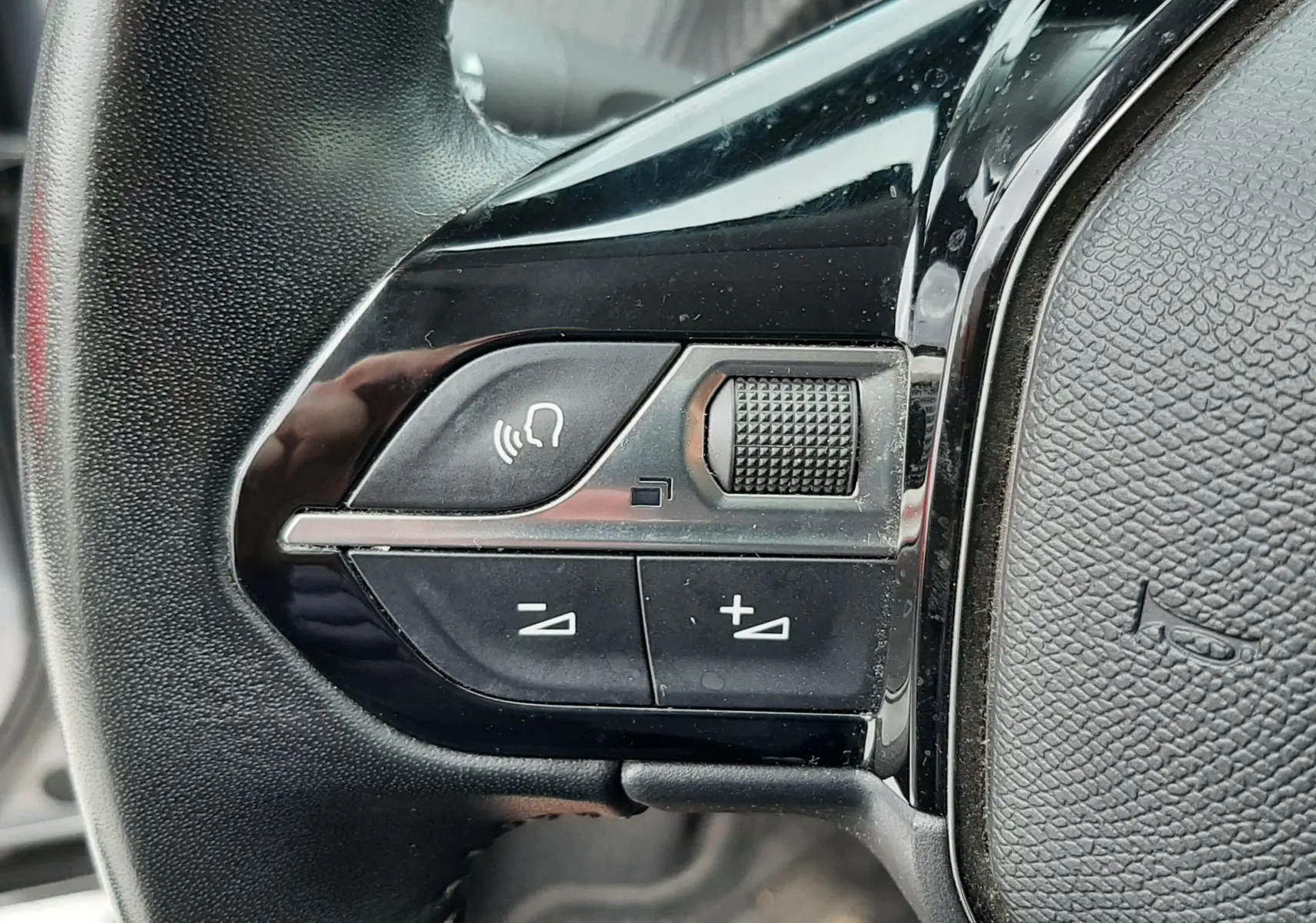 Gros plan sur les commandes de volume et téléphone au volant noir du Peugeot 2008 gris Artense, côté gauche.
