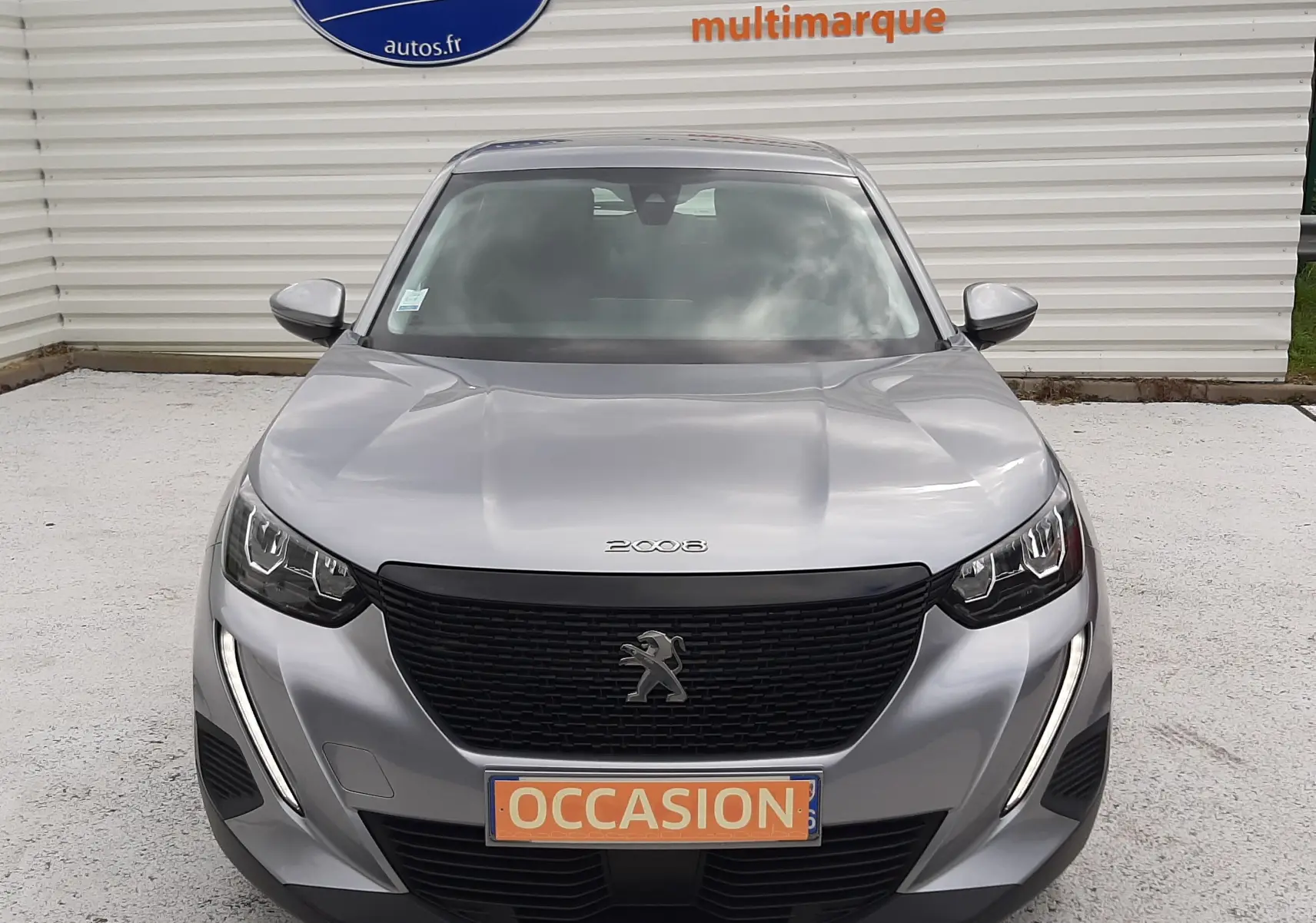 Vue de face d'un Peugeot 2008 gris Artense avec calandre noire et plaque "OCCASION" devant un mur blanc.