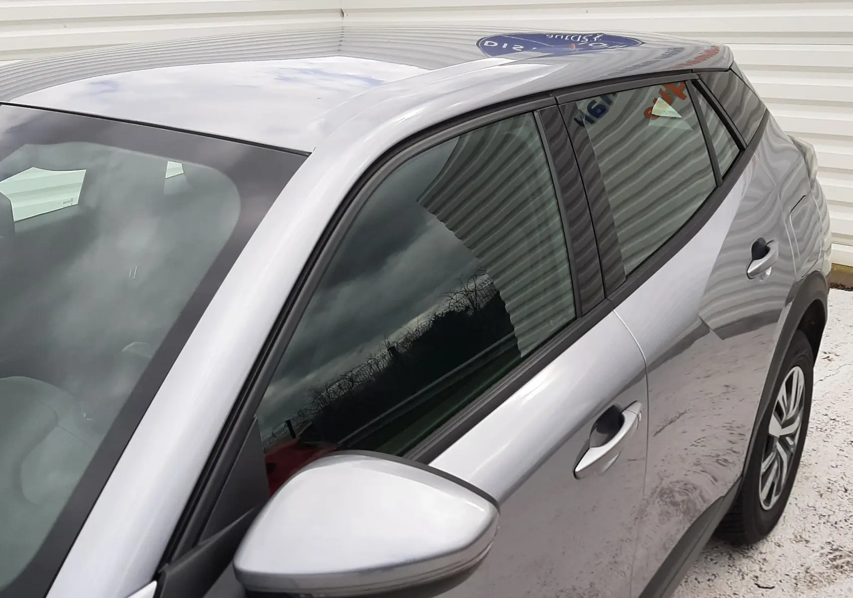 Vue rapprochée côté gauche d’un Peugeot 2008 gris Artense avec rétroviseur et vitres teintées.