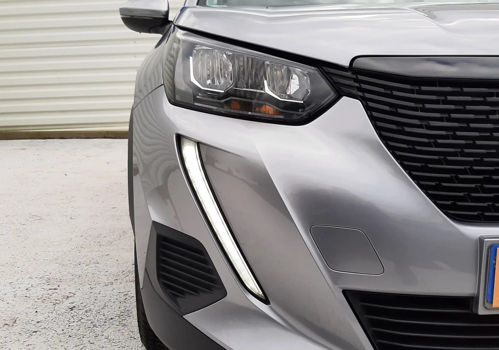 Vue rapprochée 3/4 avant gauche d’un Peugeot 2008 gris Artense mettant en valeur son phare et sa calandre noire.