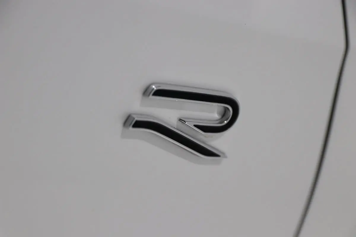 Gros plan sur l'emblème R chromé sur la carrosserie blanche d'une Volkswagen Golf 2.0 TDI 150 DSG R-Line.