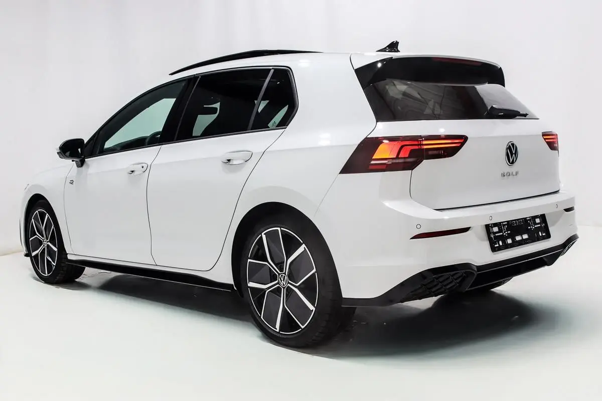 Vue 3/4 arrière droite d'une Volkswagen Golf blanche 2025 avec jantes alliage et toit panoramique noir.