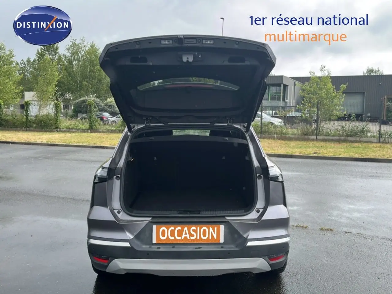 Vue arrière d'une Renault Symbioz gris cassiopée métal 2025 avec hayon ouvert montrant le coffre vide sur parking extérieur.