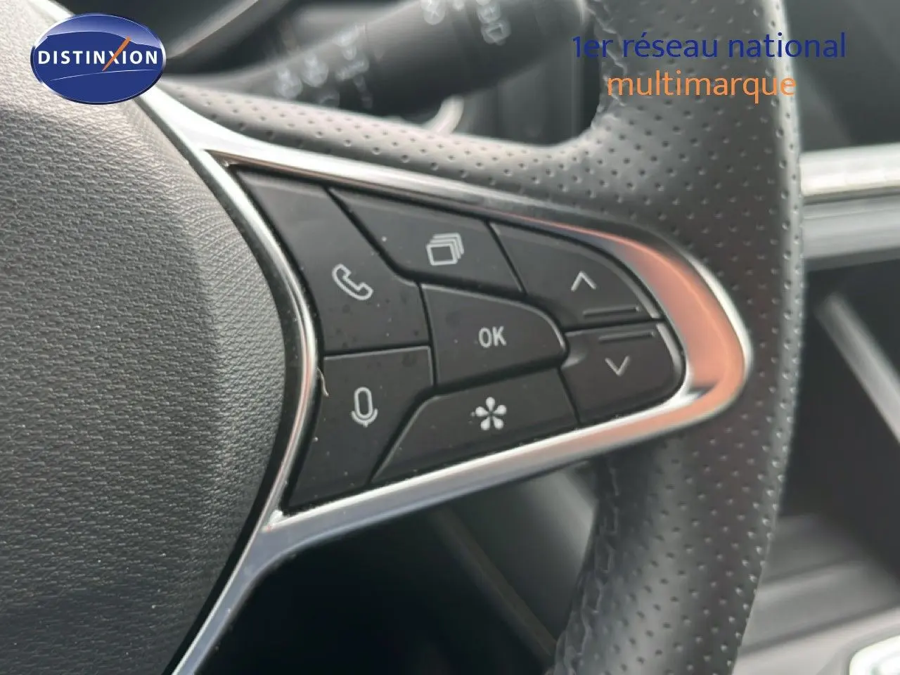 Gros plan sur les commandes multifonctions noires du volant perforé d’une Renault Symbioz gris cassiopée métal.
