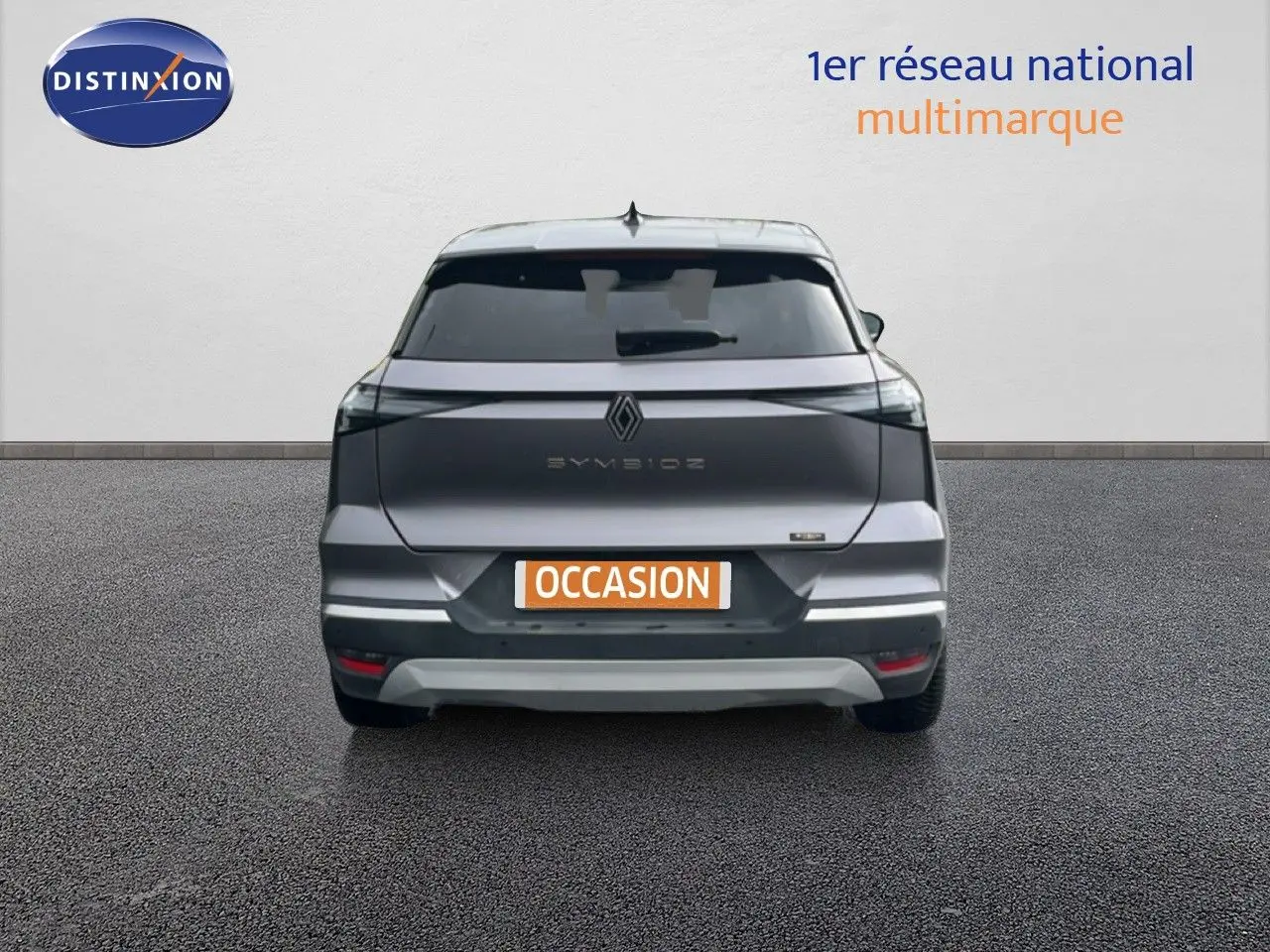 Vue arrière du Renault Symbioz gris cassiopée métal 2025 avec logo et feux LED distinctifs, en stationnement sur sol gris.