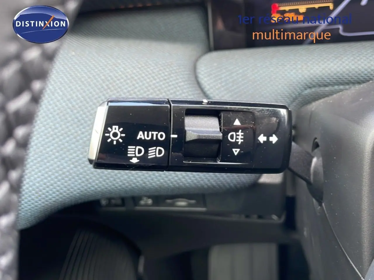 Gros plan sur la commande des feux et clignotants du Citroën C5 Aircross Hybrid 2026, avec tissu bleu clair en arrière-plan.