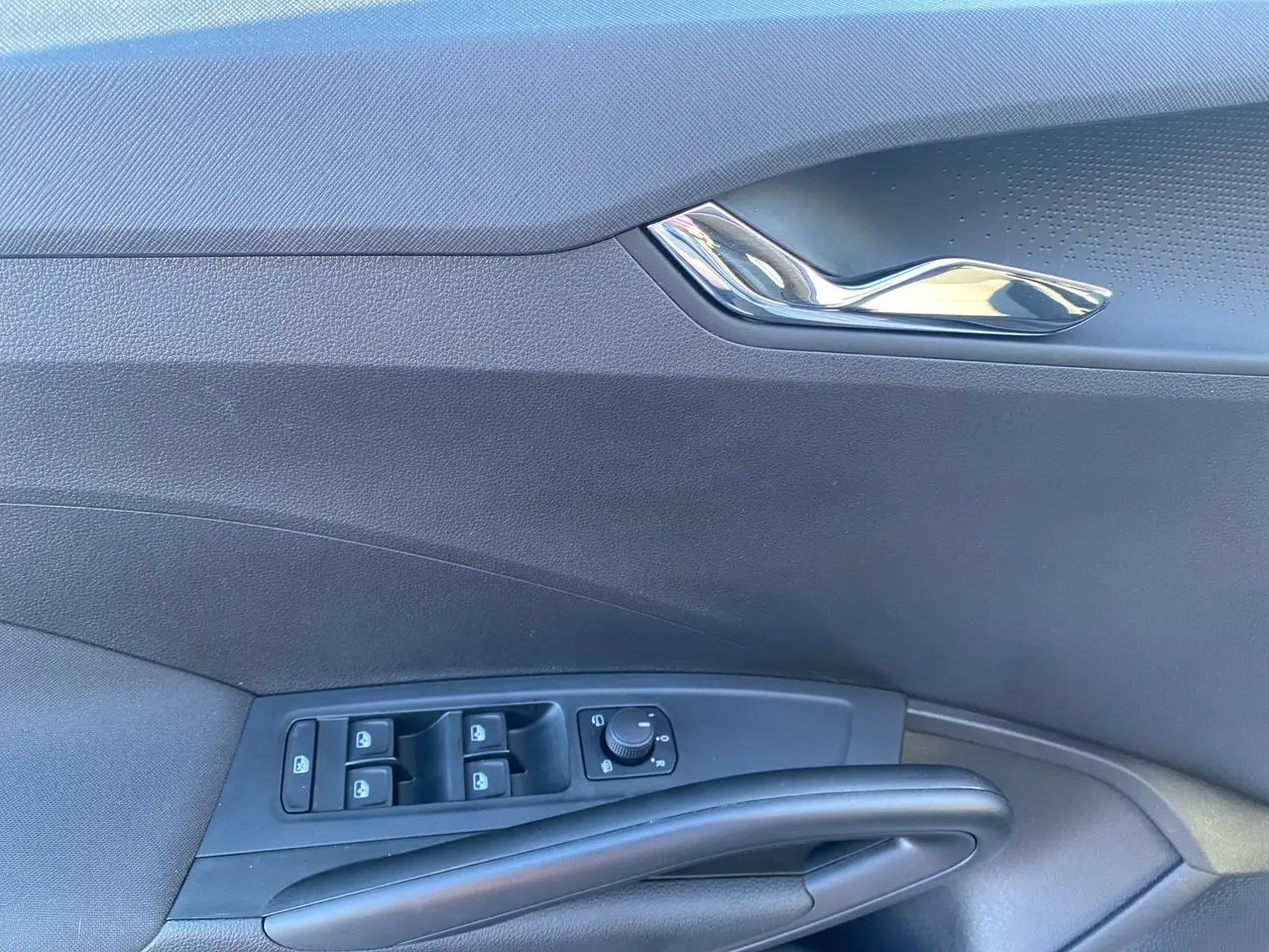 Détail de la porte côté gauche d'une Škoda Fabia 2024 gris/noir avec commandes des vitres et poignée chromée.