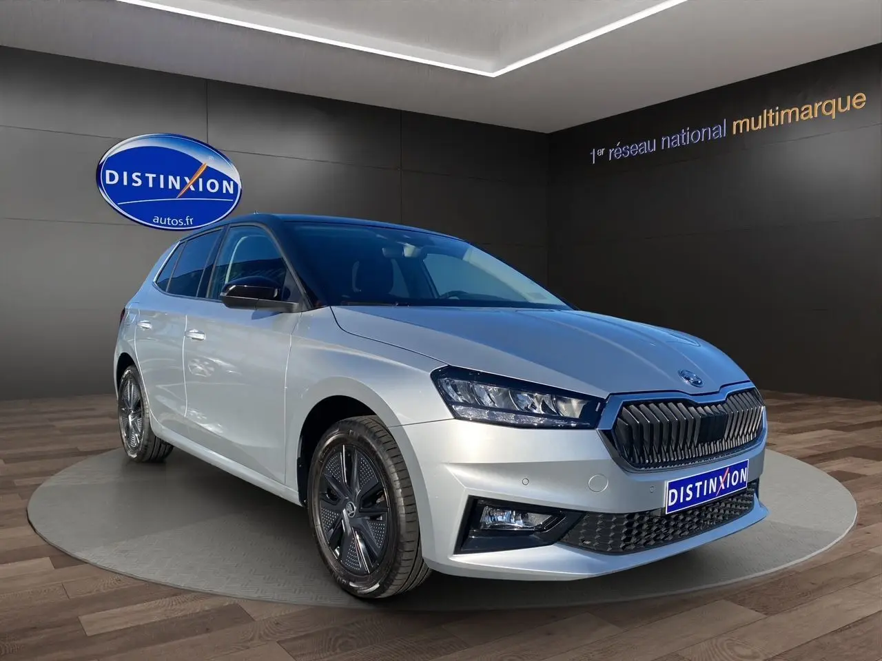 Vue 3/4 avant droite d'une Skoda Fabia 2024 gris clair avec toit et rétroviseurs noirs, calandre noire distinctive.