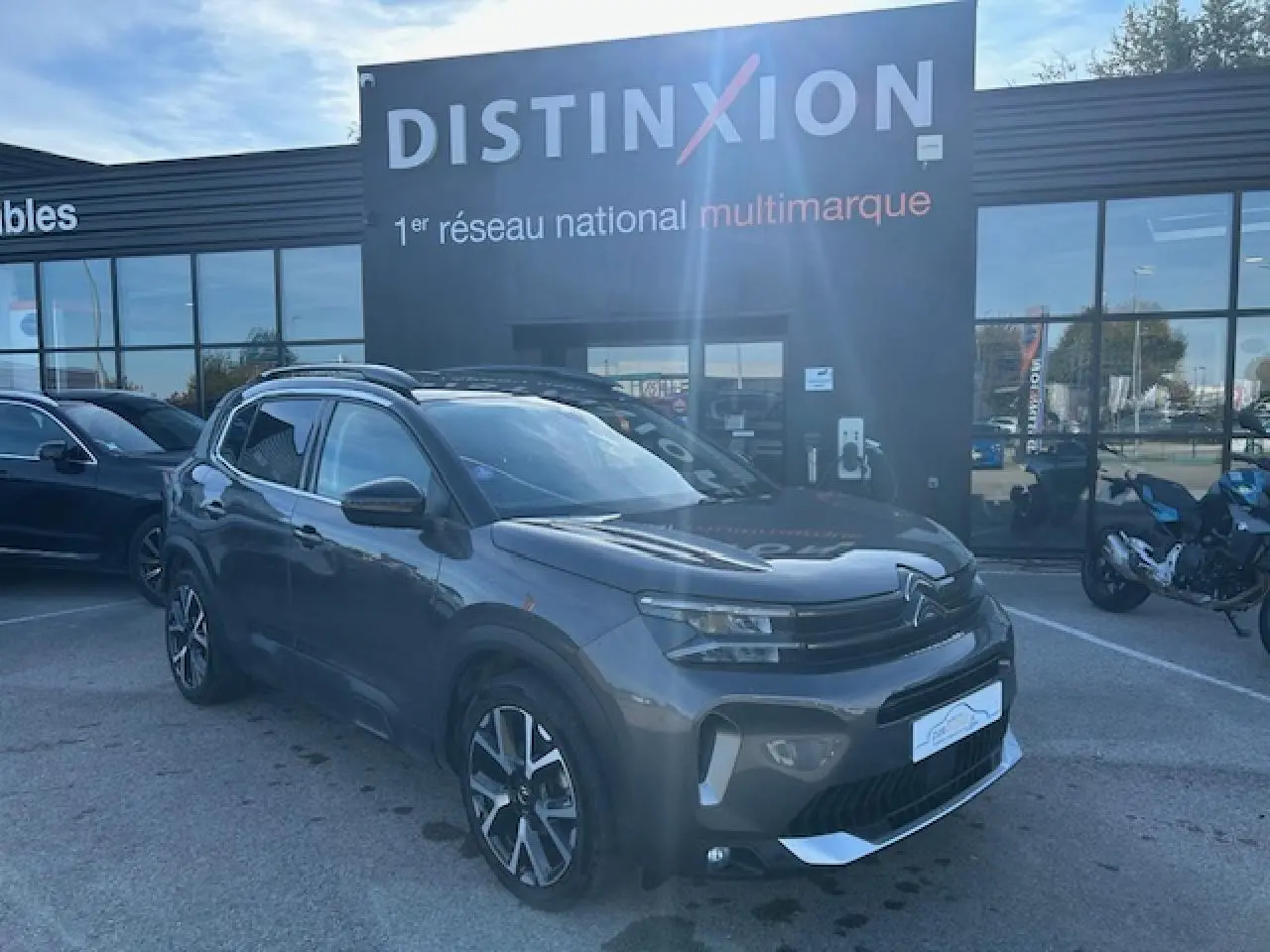 Citroën C5 Aircross gris platinium en 3/4 avant droit, avec barres de toit et jantes alliage visibles.