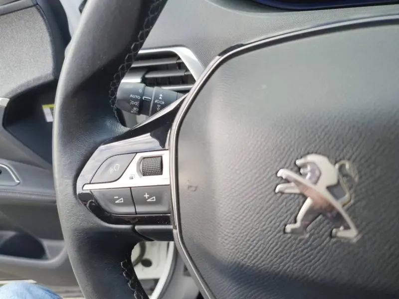 Gros plan sur le volant cuir multifonction d'un Peugeot 3008 blanc nacré, avec commandes audio intégrées côté gauche.