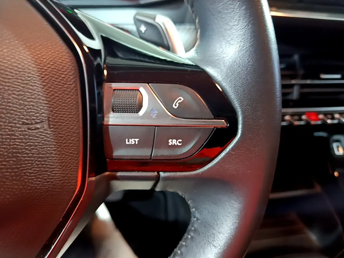 Gros plan sur le volant cuir noir multifonctions du Peugeot 2008, avec commandes audio et téléphone intégrées.