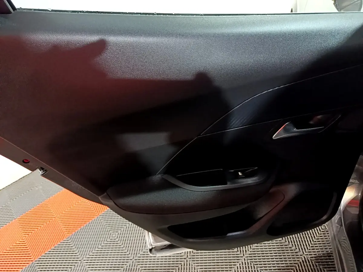 Vue intérieure du panneau de porte côté gauche du Peugeot 2008 gris clair, avec poignée argentée et commande de lève-vitre.