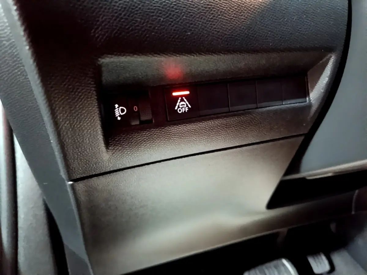 Gros plan sur les commandes noires du tableau de bord gauche du Peugeot 2008 gris clair, avec témoin d'alerte allumé.