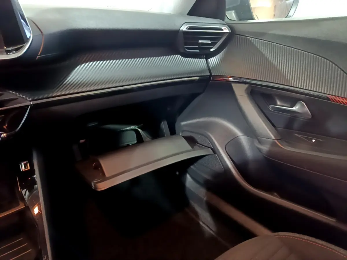 Intérieur côté passager du Peugeot 2008 gris clair, vue sur la boîte à gants ouverte et le tableau de bord noir avec inserts carbone.