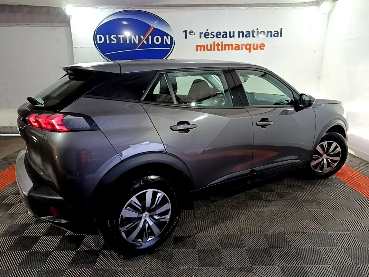 Peugeot 2008 gris clair vue 3/4 arrière droit en intérieur, avec feux arrière LED et jantes alliage.