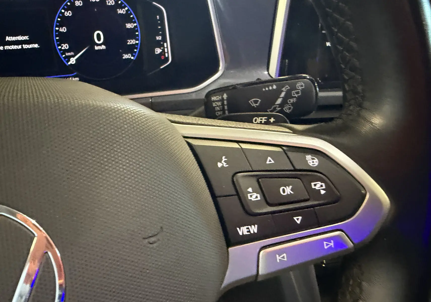 Gros plan sur le volant noir du Volkswagen T-Roc bleu 2022, avec commandes multifonctions et tableau de bord digital.