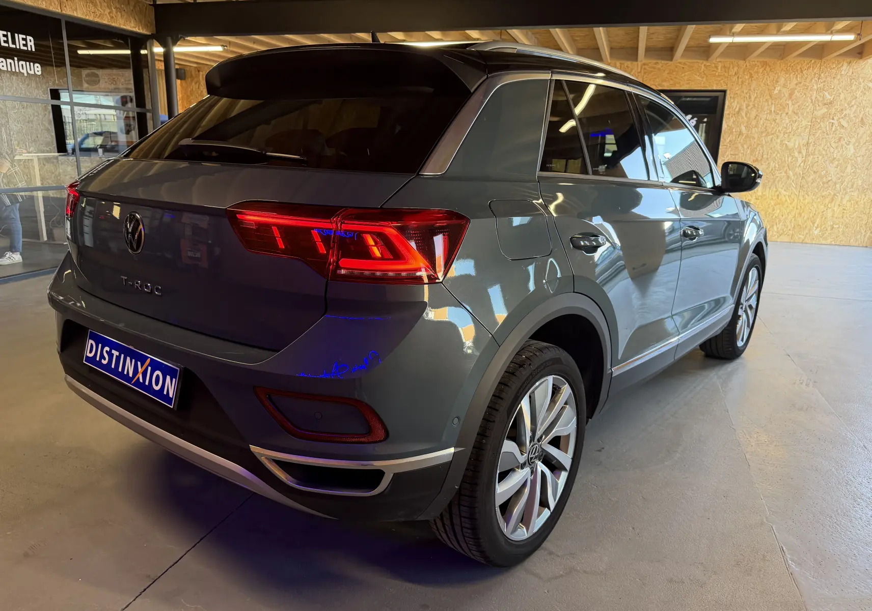 Vue 3/4 arrière droite d’un Volkswagen T-Roc gris métallisé 2022 avec feux arrière allumés, en intérieur showroom.