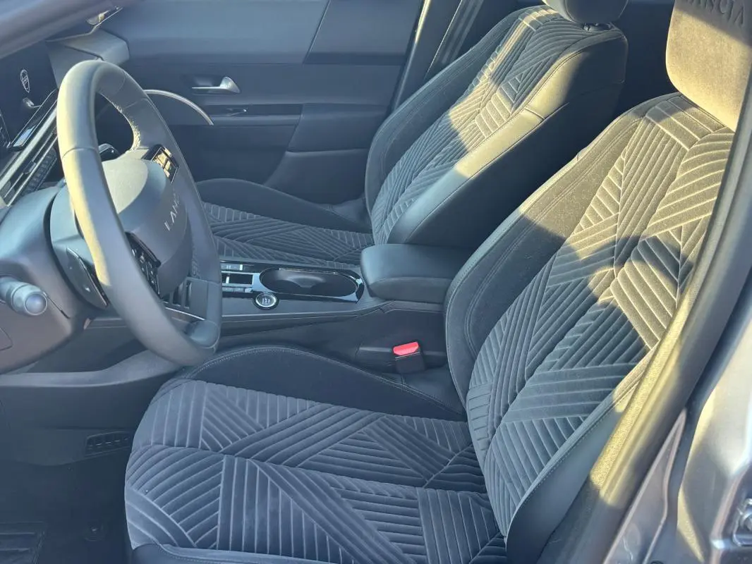 Vue intérieure côté conducteur de la Lancia Ypsilon gris 2025, sièges en tissu à motifs géométriques et volant sport.