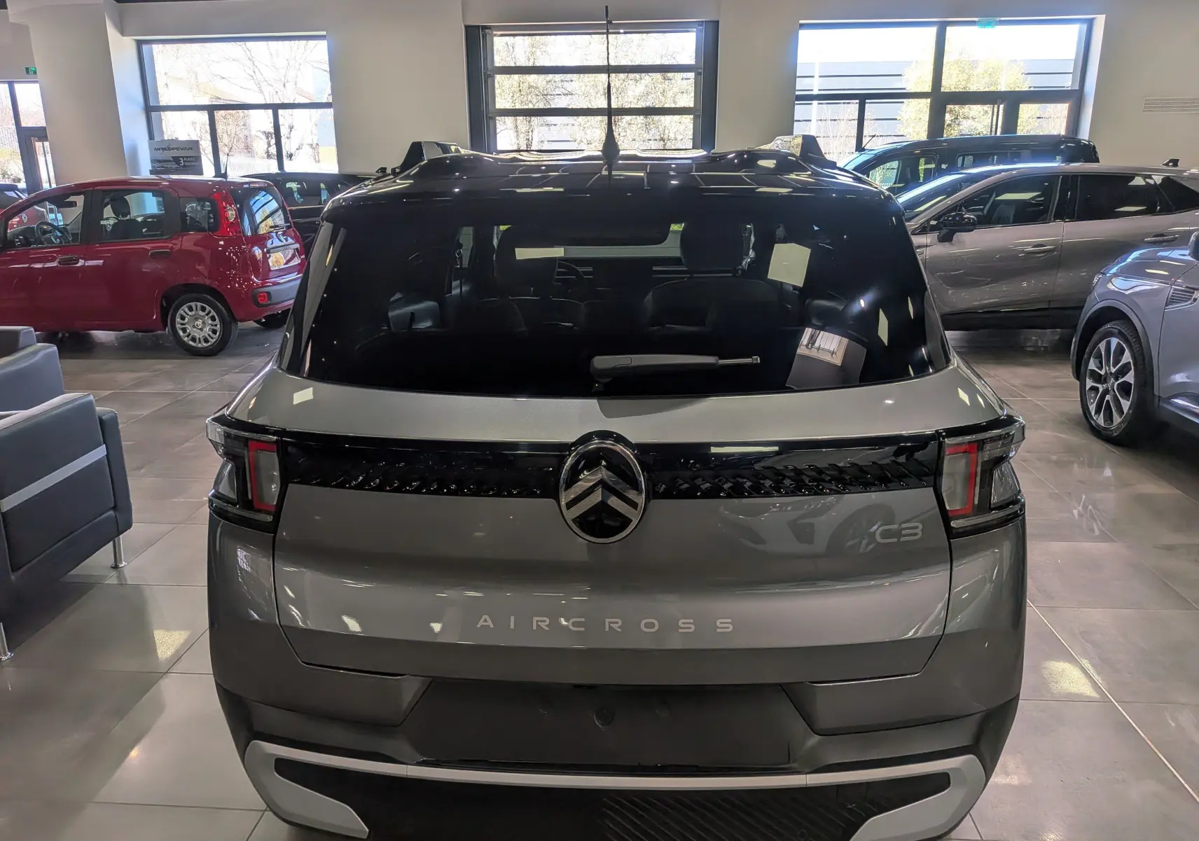 Vue arrière d’un Citroën C3 Aircross hybride 2026 gris Mercury avec toit noir en showroom, mettant en valeur son logo et ses feux distinctifs.