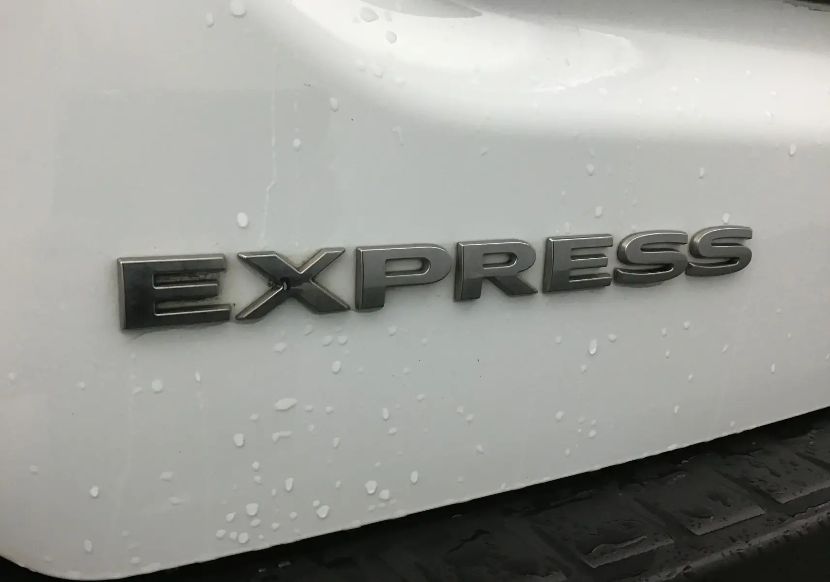 Gros plan sur l’inscription Express en lettres métalliques sur la partie arrière blanche du Renault Express Van.