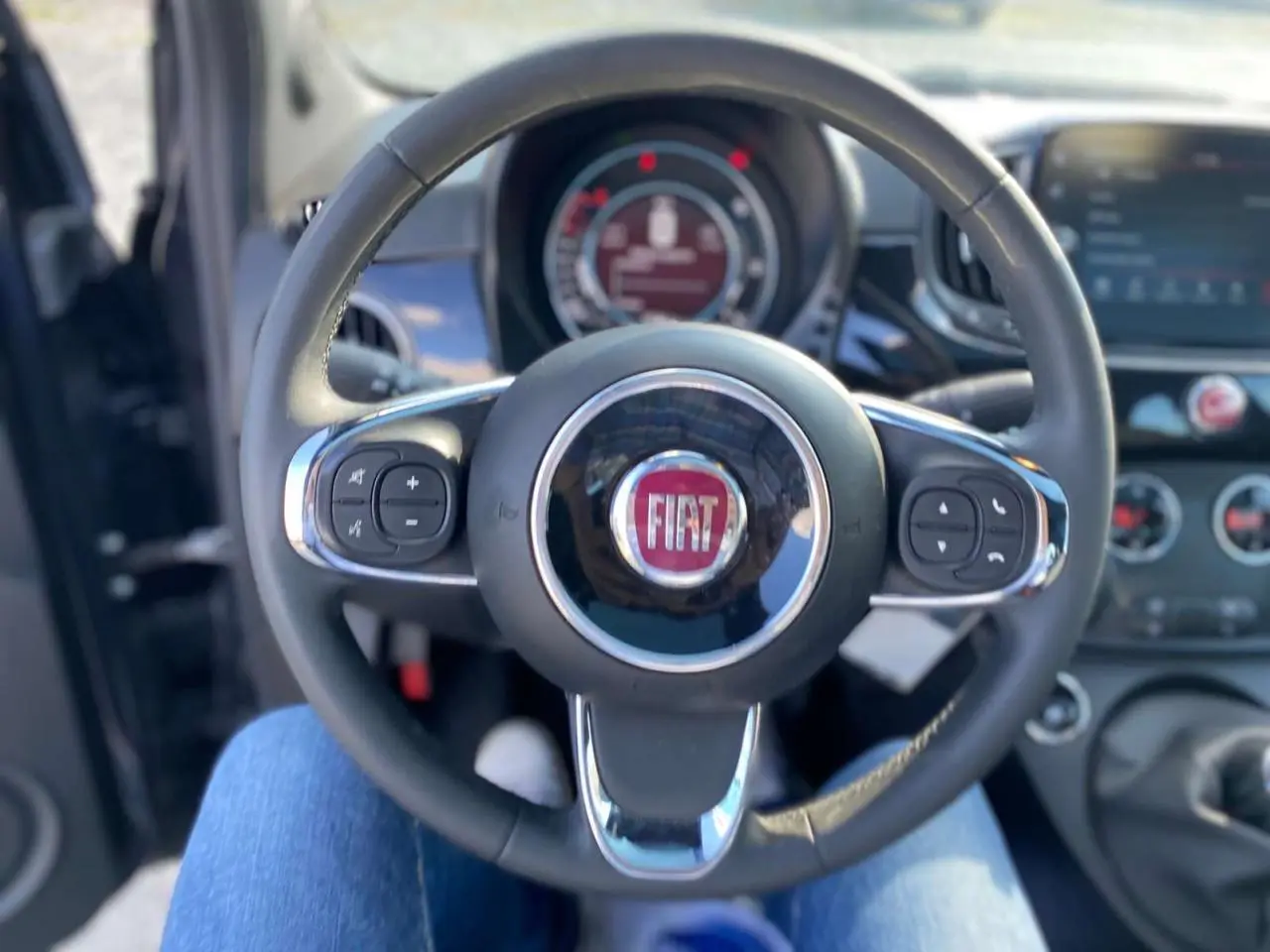 Vue centrée sur le volant noir du Fiat 500 2024 avec commandes intégrées et tableau de bord en arrière-plan.