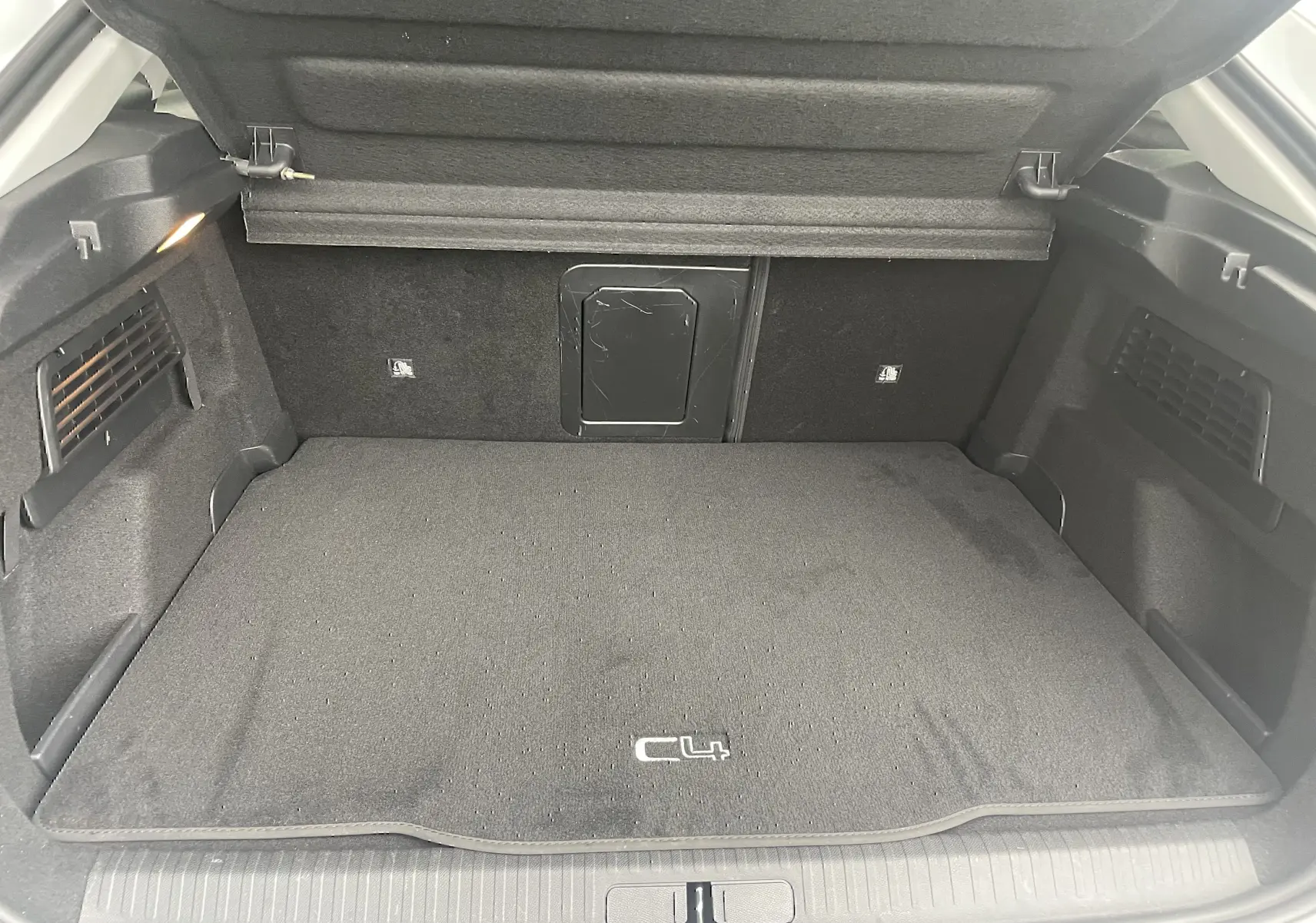 Coffre ouvert d'une Citroën C4 blanche 2022, vue intérieure montrant un tapis noir avec logo C4 et éclairage latéral.