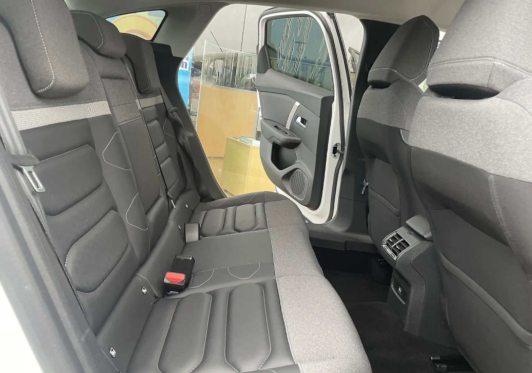 Vue intérieure arrière côté gauche d'une Citroën C4 blanche 2022, sièges tissu gris noir avec porte ouverte.