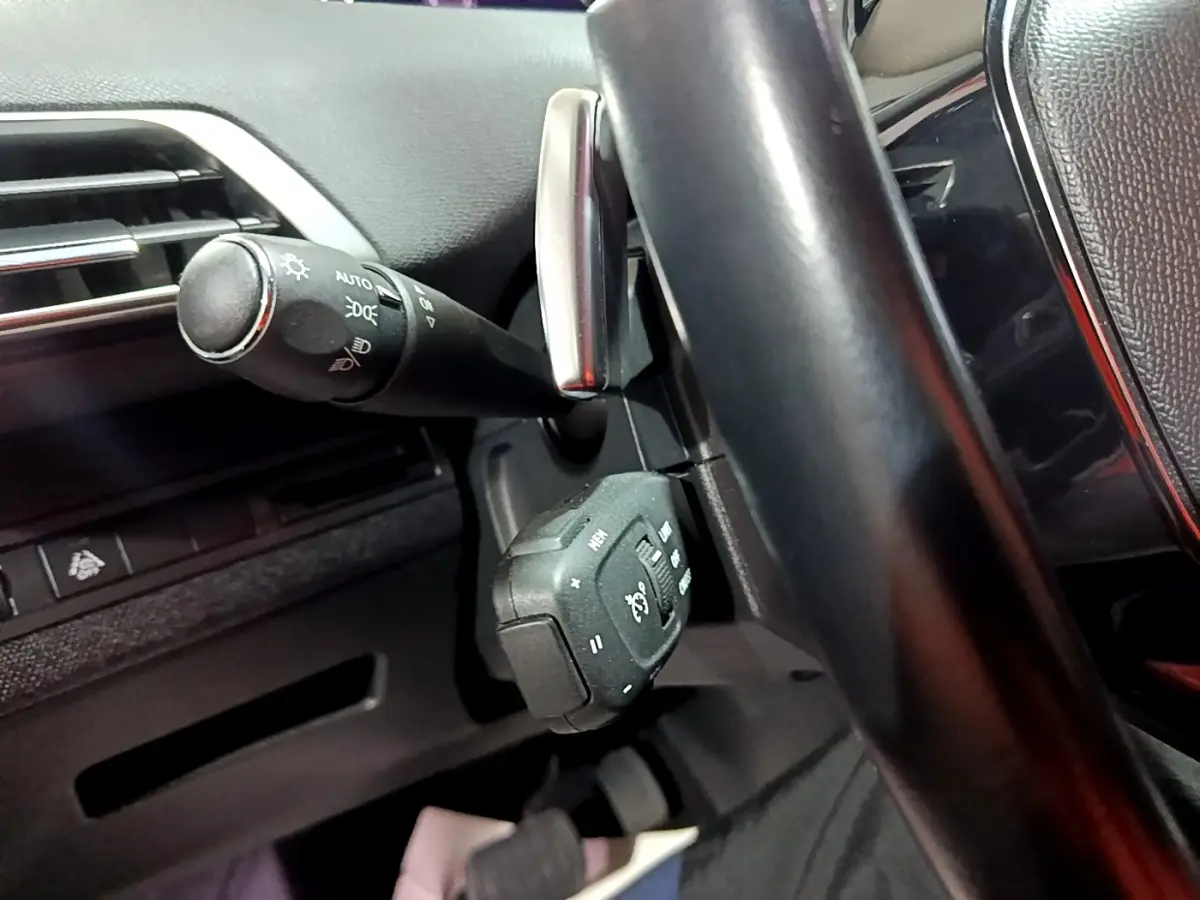 Gros plan sur la commande multifonctions et la manette des phares derrière le volant cuir noir du Peugeot 3008 2022.