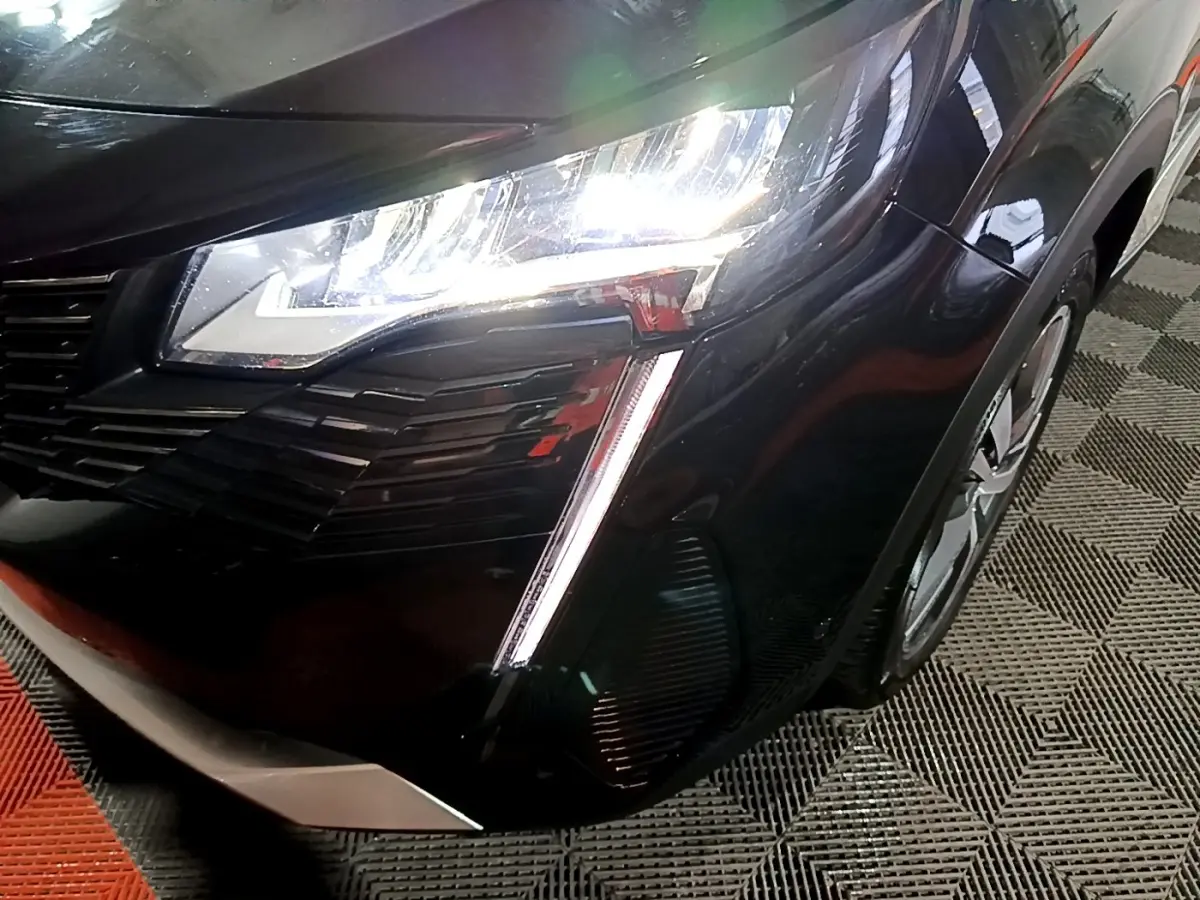 Gros plan sur l'avant droit noir du Peugeot 3008 2022 avec phares LED allumés et calandre distinctive.