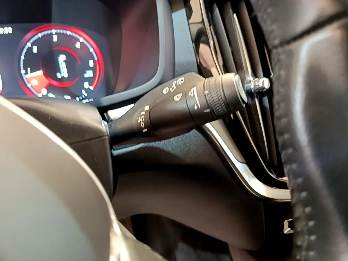 Détail du commodo d’essuie-glace côté gauche avec tableau de bord numérique rouge et noir d’une Volvo V60 2020.