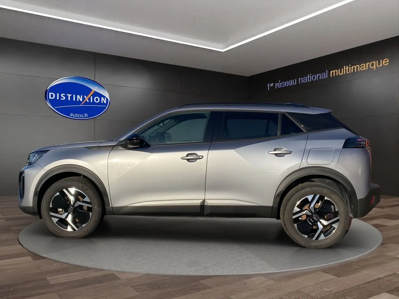 Peugeot 2008 gris Artense vue de profil côté gauche, avec jantes noires et toit foncé en intérieur showroom.