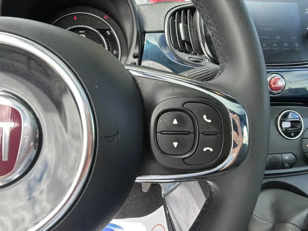 Gros plan sur les commandes au volant du FIAT 500 bleu 2024, avec tableau de bord et ventilation visibles en arrière-plan.