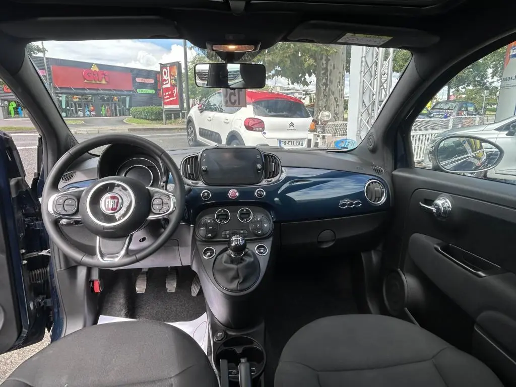 Vue intérieure avant du Fiat 500 bleu 2024 avec tableau de bord brillant, volant multifonction et levier de vitesses manuel.