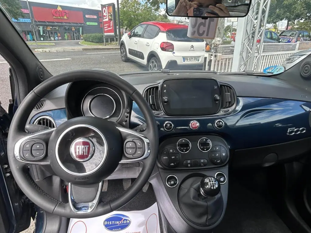 Vue intérieure avant du tableau de bord bleu et volant multifonction du FIAT 500 2024 avec boîte manuelle et écran tactile central.
