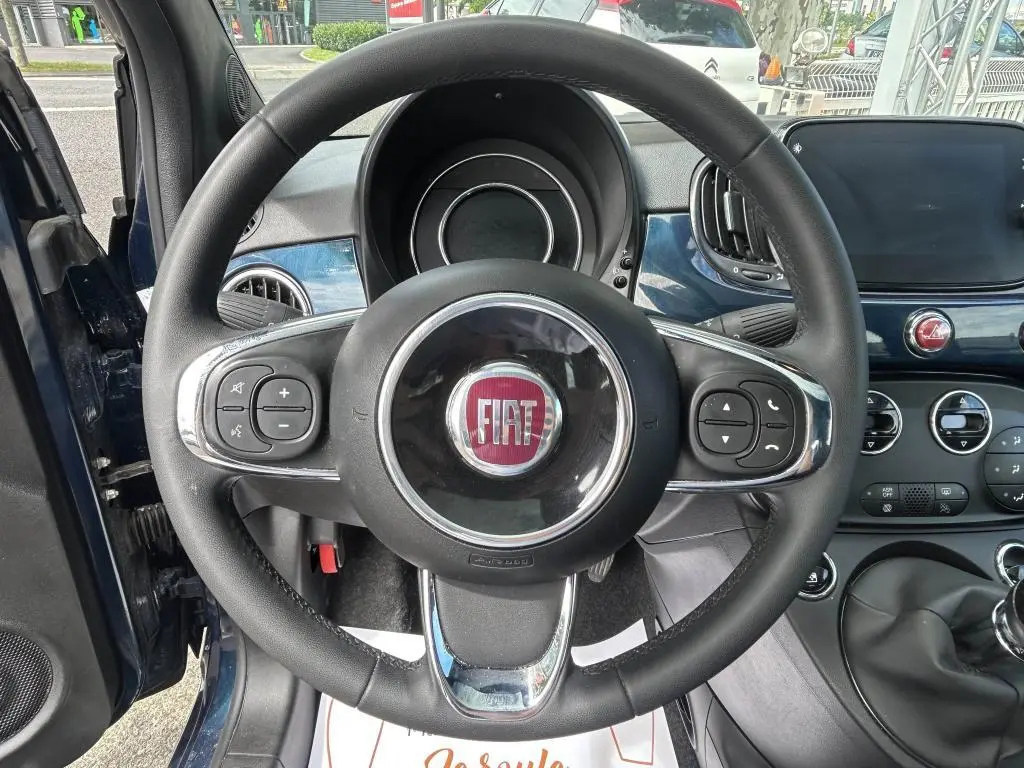 Vue intérieure centrée sur le volant de la Fiat 500 bleu 2024 avec commandes au volant et tableau de bord assorti.