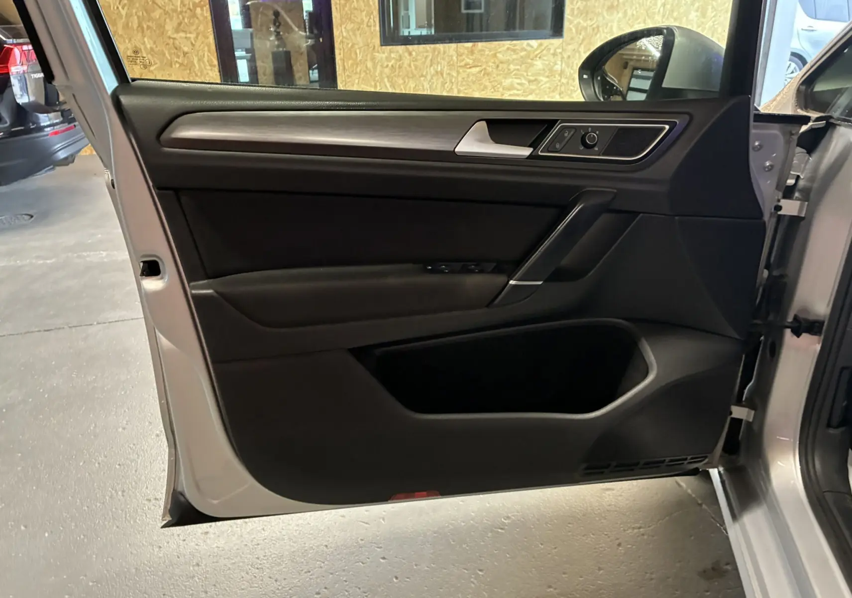 Porte avant gauche ouverte d'une Volkswagen Golf Sportsvan gris, montrant la garniture intérieure noire avec commandes de vitres et rétroviseur.