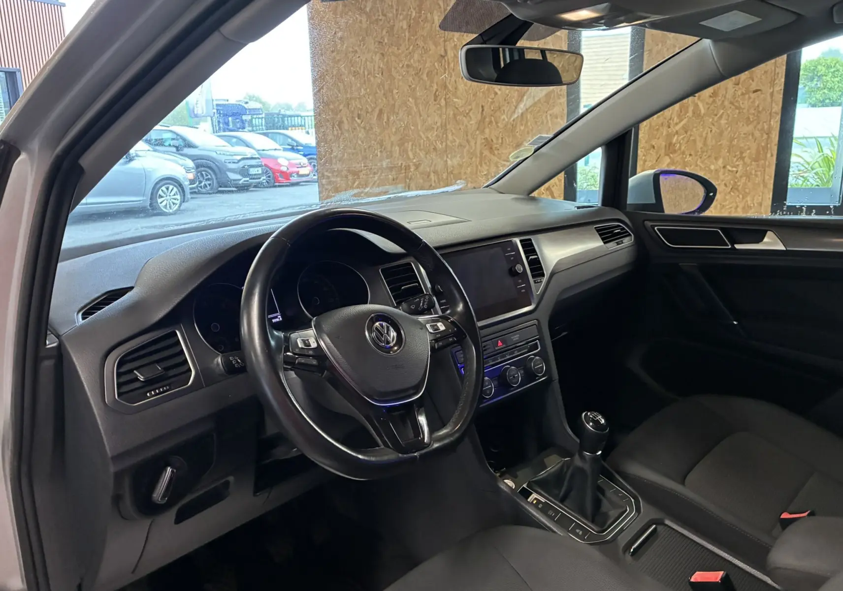 Vue intérieure côté conducteur de la Volkswagen Golf Sportsvan gris 2019, volant multifonction et boîte manuelle visibles.