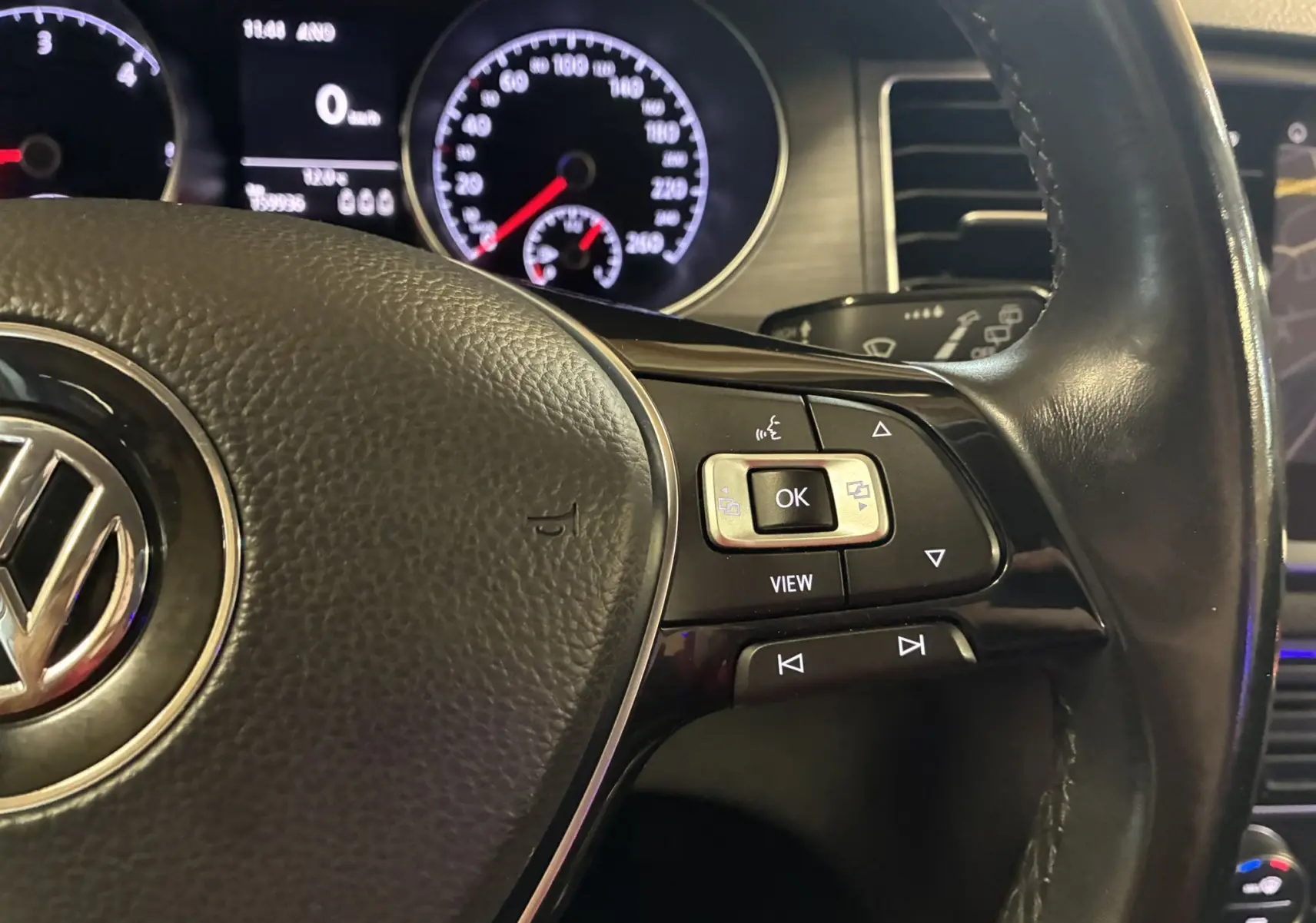 Gros plan sur le volant en cuir noir de la Volkswagen Golf Sportsvan 2019 avec commandes multifonctions et tableau de bord éclairé.